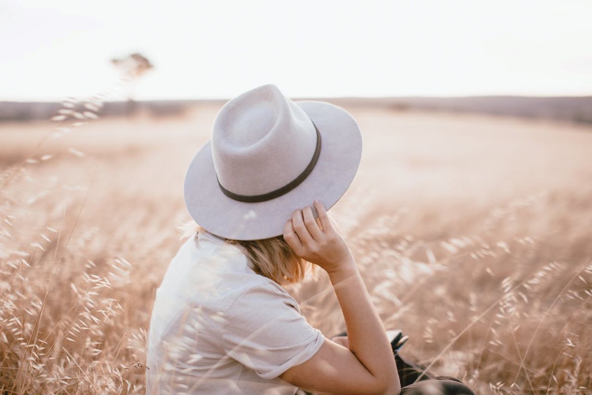 A woman in a hat sits peacefully in a lush green field, immersed in personal testaments of faith.