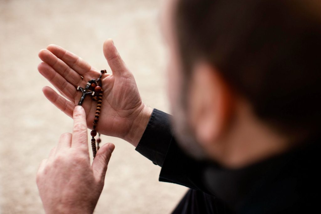 A man examining the rosary beads he’s holding.