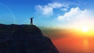 A man watching the sun rise while atop a mountain who overcomes the world