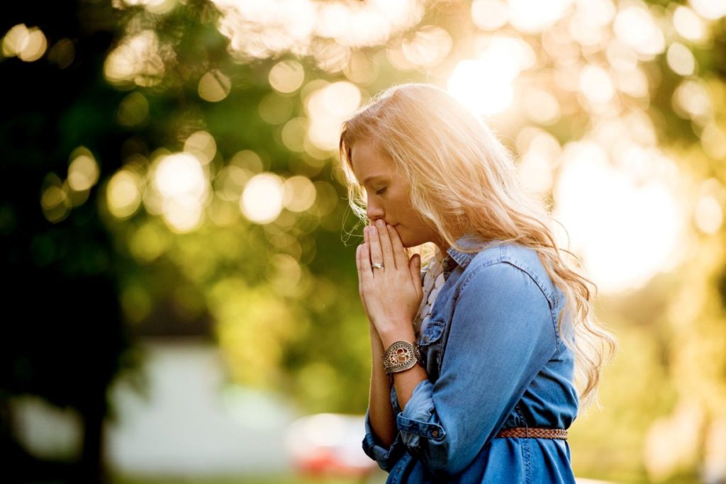 A woman praying as the sun shines on her.