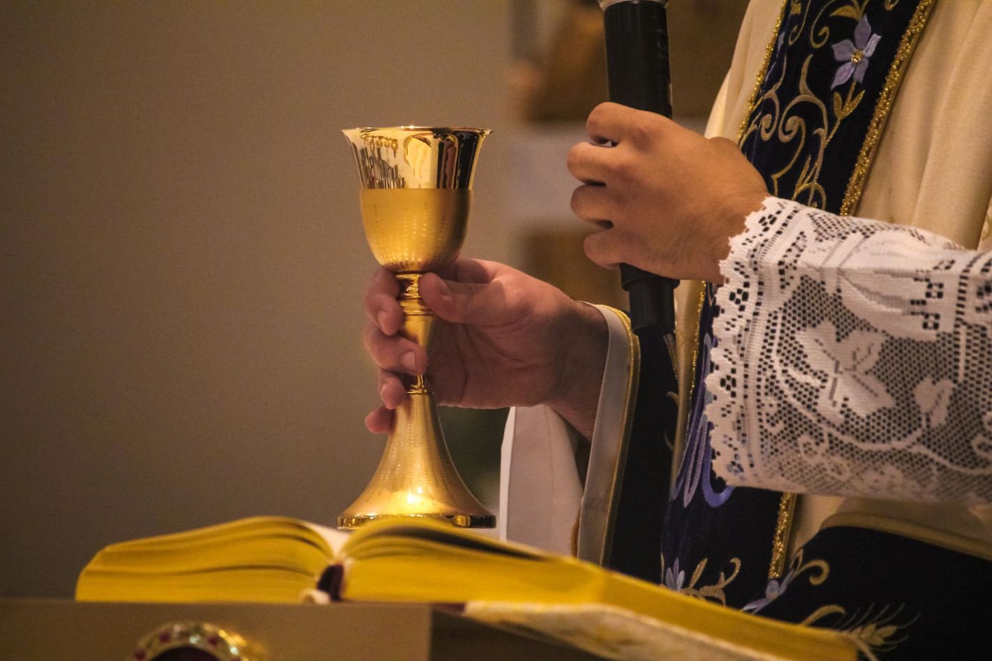 Priest holding a chalice and a microphone.